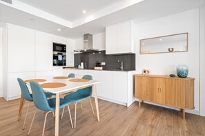 A modern kitchen with white cabinetry, a wooden dining table with blue chairs, and a wooden sideboard with decorative items. - Stylish Couple Retreat in Casares (Casares)