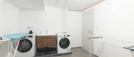 A laundry room with two washing machines, a drying rack, and a small ironing station.