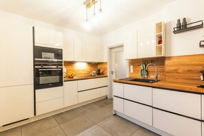 A modern kitchen with white cabinets, a built-in oven, a wooden countertop, and a sink. - Family-friendly vacation home in Winterberg with sauna, hot tub & play area (Winterberg)