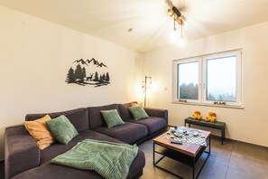 A living room with a sofa, a coffee table, and a wall decoration. - Family-friendly vacation home in Winterberg with sauna, hot tub & play area (Winterberg)