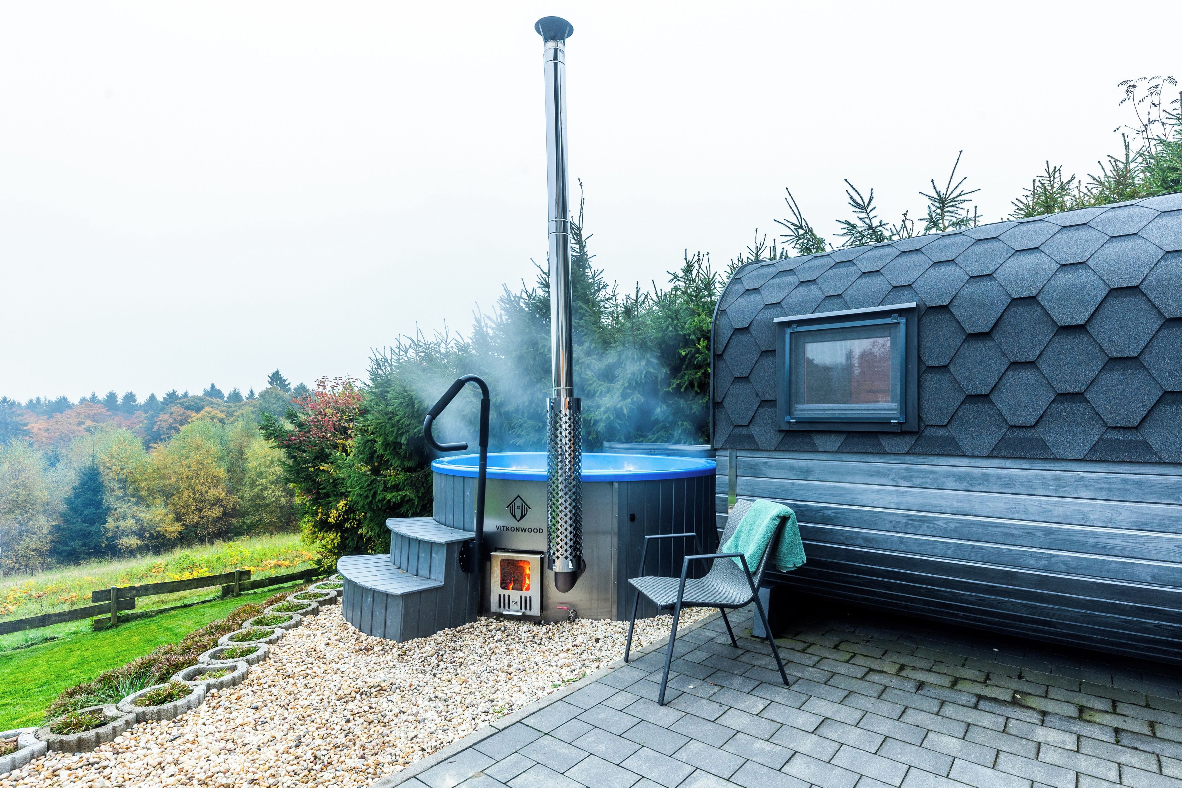 A hot tub with a chimney, a deck chair, and a hexagonal building with a window.