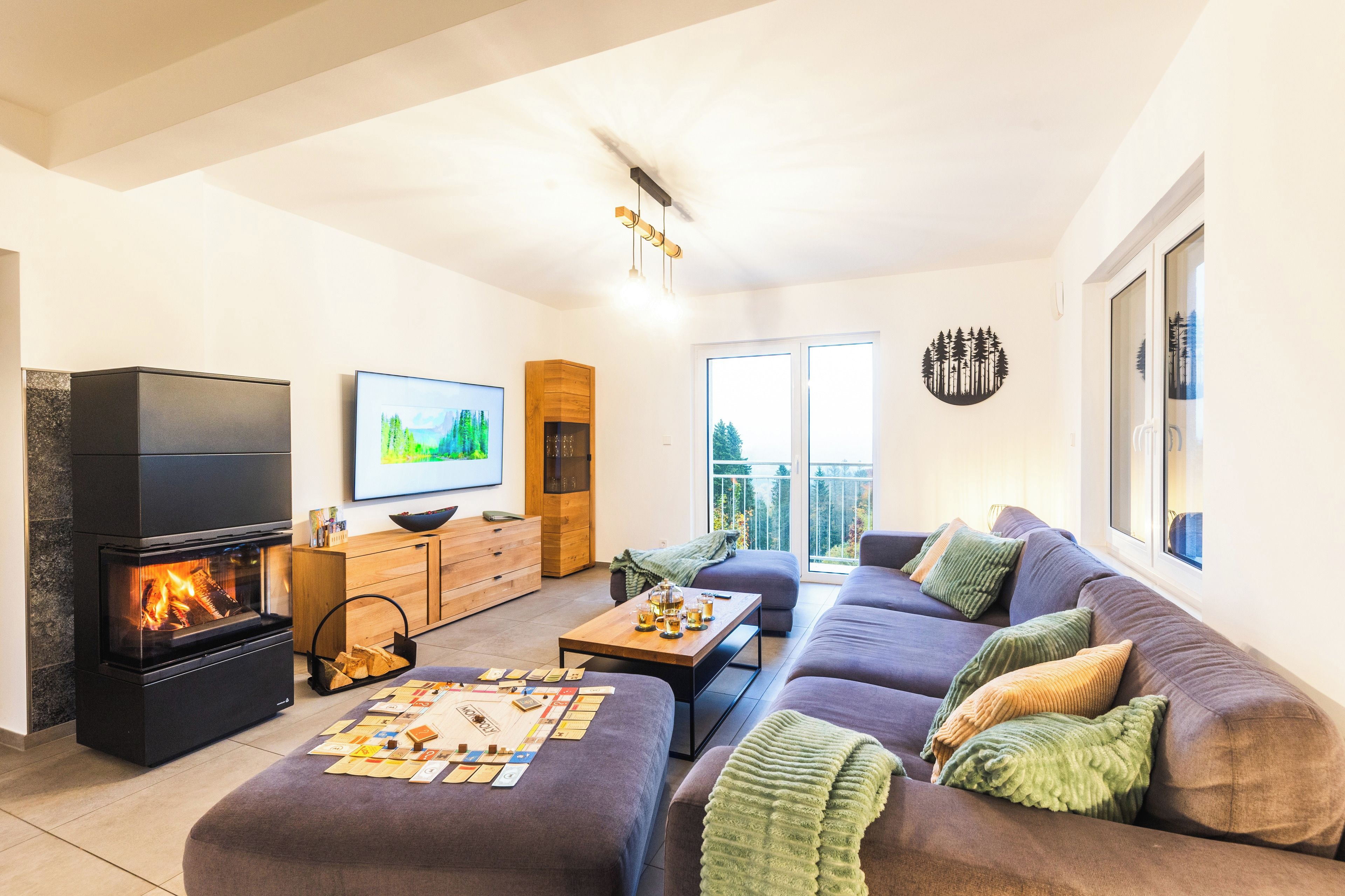 Ein modernes Wohnzimmer mit Kamin, Flachbildfernseher, einer Sofagarnitur und einem Esstisch mit Gesellschaftsspielen.