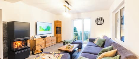 A modern living room with a fireplace, a flat-screen TV, a sofa set, and a dining table with board games.