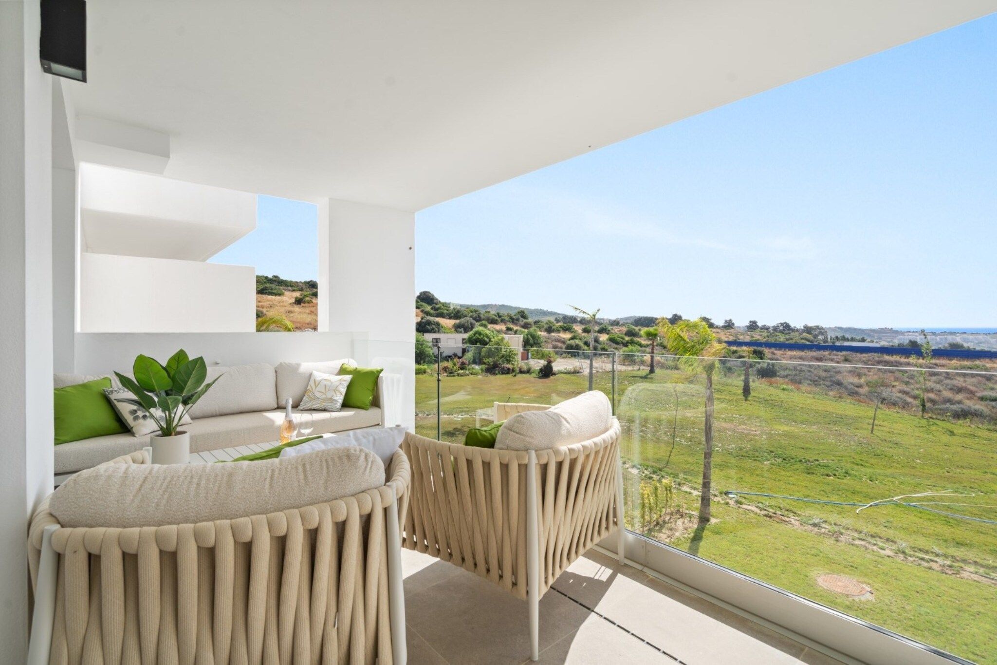 Un balcon moderne avec un canapé et des fauteuils, une plante en pot et une vue sur un paysage verdoyant.