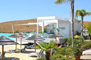 Un hotel junto a la playa con piscina, sillas de descanso y sombrillas.