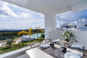 A balcony with a dining table set for two, overlooking a swimming pool and a view of the surrounding landscape. - Stylish Lagoon Apartment for 4 (Casares)