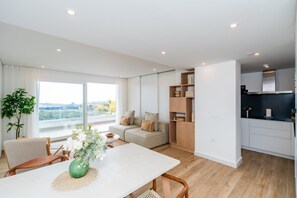 A modern apartment with a dining area, sofa, kitchen, and large windows offering a view. - Stylish Lagoon Apartment for 4 (Casares)