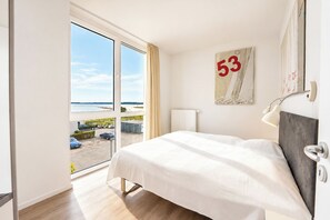 Quarto de hotel com uma grande janela, uma cama, um letreiro com número na parede e vista para o exterior.