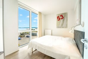 A hotel room with a large bed, a view of the sea through a sliding door, a number '53' on the wall, and a modern lamp. - Promenade Villa 03 Apartment 09 (Lübeck-Travemünde)