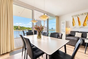A modern dining area with a large table, chairs, and a view of a body of water and buildings. - Villa Promenade 03, Apartment 09 (Lübeck-Travemünde)