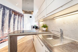 A modern kitchen with a central island, stainless steel sink, and a backsplash with a unique pattern. - Villa Promenade 03, Apartment 09 (Lübeck-Travemünde)