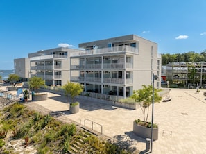 A modern multi-story building with balconies, a paved courtyard, and a beach view. - Villa Promenade 03, Apartment 09 (Lübeck-Travemünde)