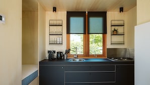 Cocina compacta con isla central, ventana con persianas y estanterías empotradas con vasos y una planta.