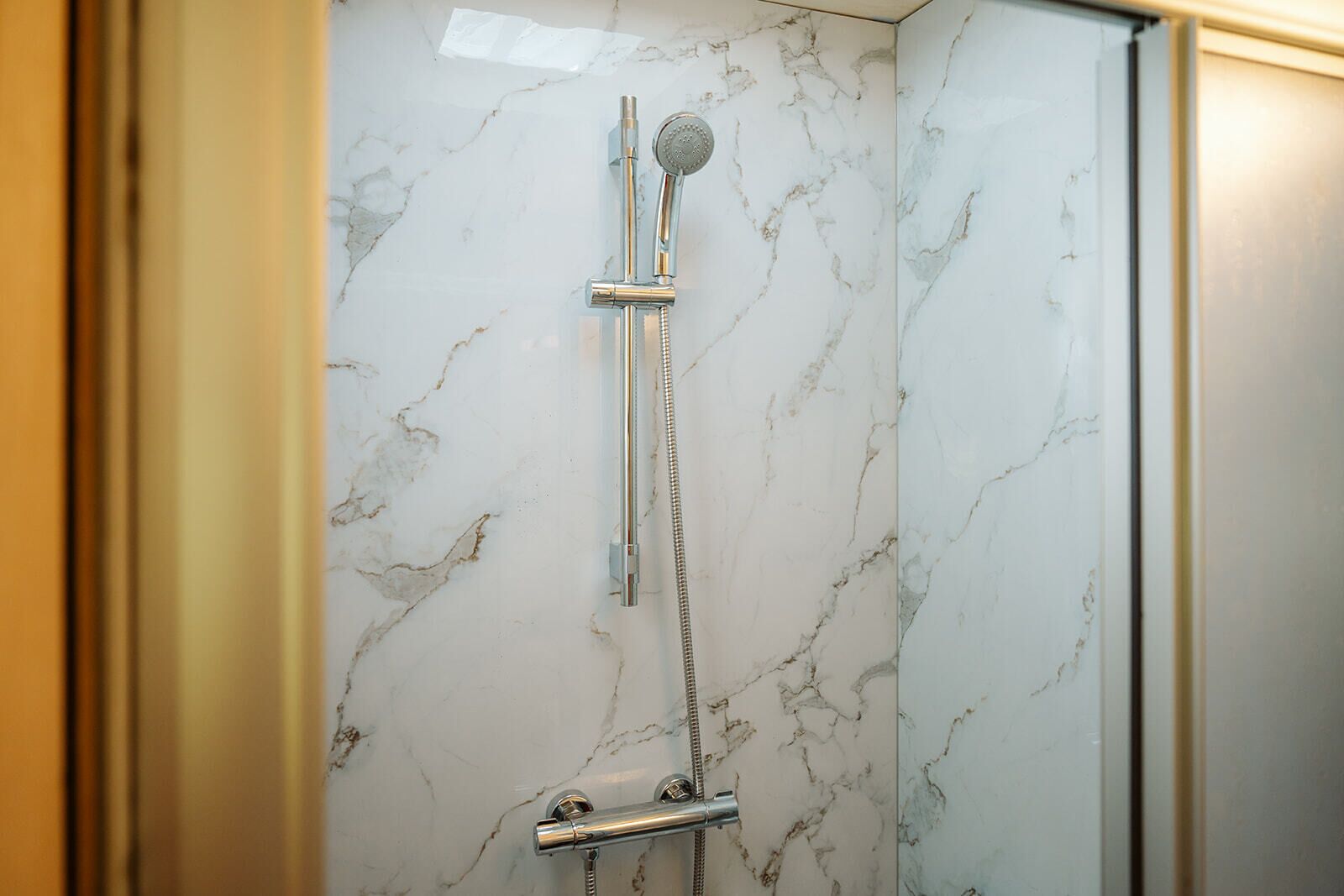 A bathroom with a shower, marble walls, and a glass door.