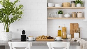Et moderne køkken med hvide skabe, en kaffemaskine, en bakke med småkager og en potteplante.