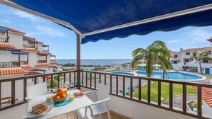 Ein Balkon mit Frühstückstisch, mit Blick auf einen Swimmingpool und das Meer.