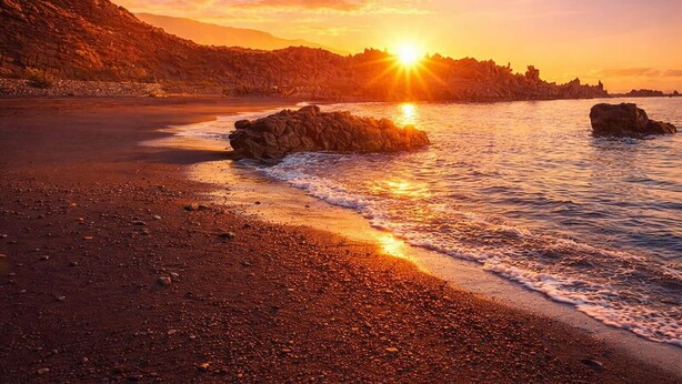 Ein Strand mit Felsformationen und einem Sonnenuntergang.