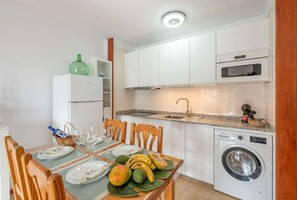 A modern kitchen with white cabinets, a built-in oven, and a washing machine. - Cascajos Beachfront Apartment for 3 (Breña Baja)
