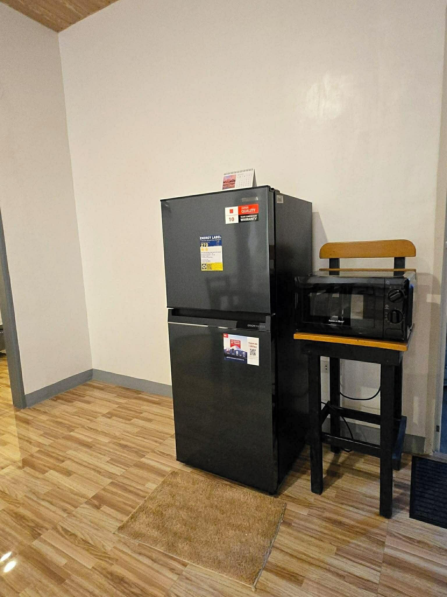 A black refrigerator with energy labels and a wooden bench beside it.