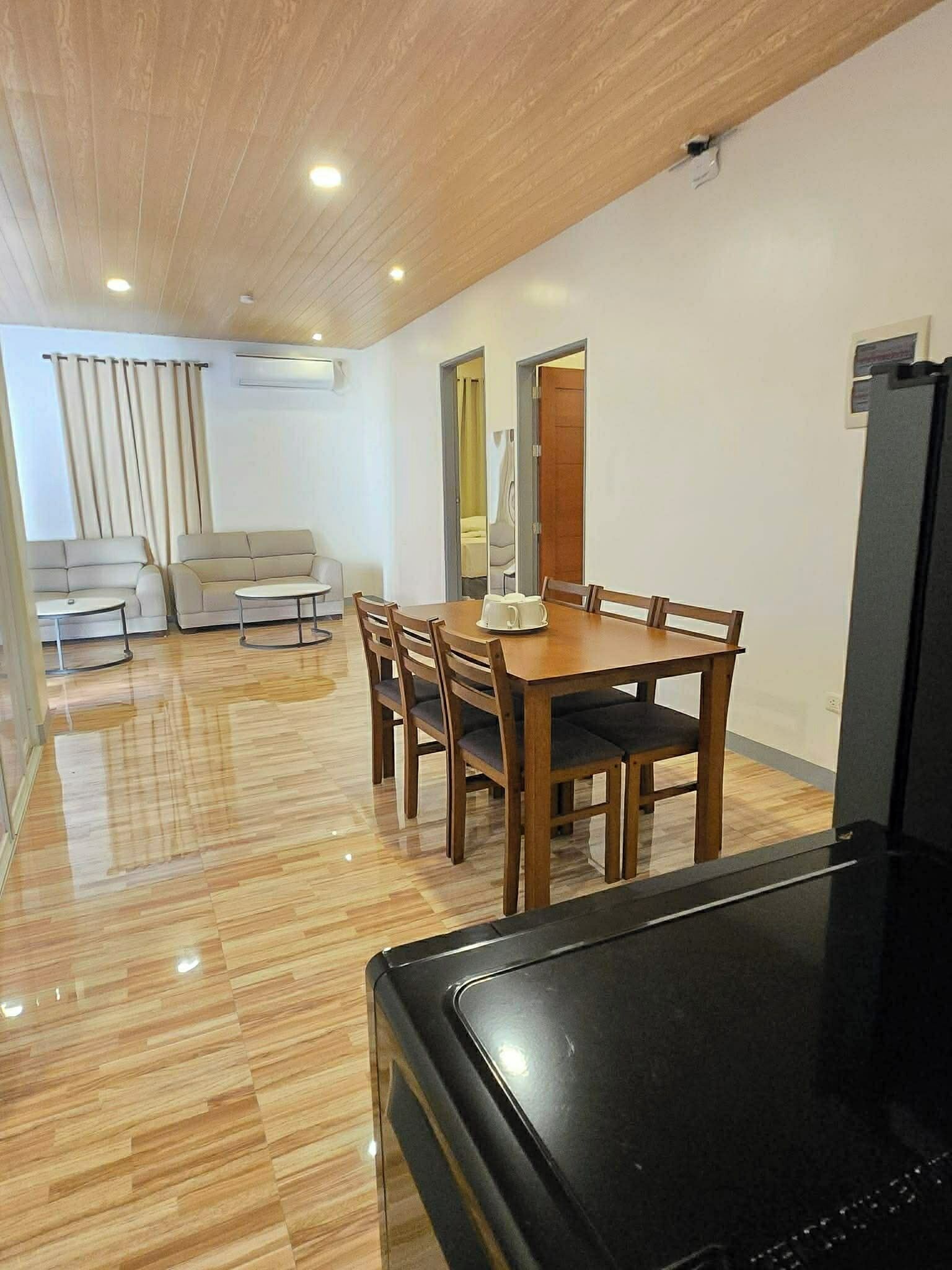 A dining area with a wooden table and chairs, a sofa, and a television.