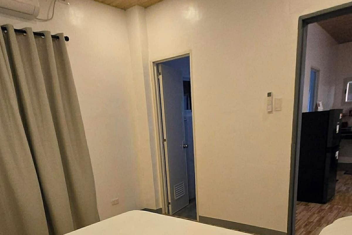 A hotel room with a neatly made bed, a door leading to another room, and a visible air conditioning unit.