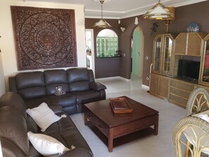 A living room with a brown leather sofa, a wooden coffee table, and a large decorative panel on the wall. - Chalet El Bucanero – Morro Jable, La Cornisa (Solana Matorral)