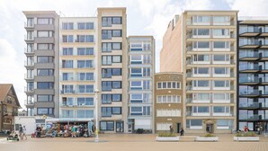 A modern apartment building with multiple balconies, a ground-level retail space, and a paved plaza area. - 3 bedroom accommodation in Nieuwpoort (Nieuwpoort)