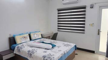 Um quarto com cama, mesas de cabeceira, ar condicionado, janela com persianas e uma porta.