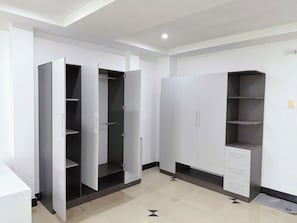 A room with a wardrobe, open closet, and a cabinet with drawers.