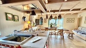 A kitchen with a central island, wooden cabinets, and a red stove. There is a dining area with a table and chairs, and a sofa in the background.