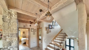 A spacious hallway with a stone wall, wooden ceiling, and a staircase with a wooden railing.