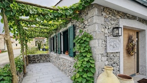 A stone building with a pergola covered in green vines, a stone wall, and a wooden door. - Luxury Villa Kras 5 Bedrooms Outdoor Kitchen Near Trieste (Dutovlje)