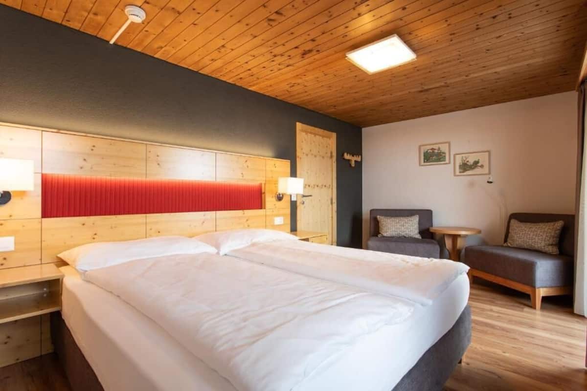 Ein Hotelzimmer mit einem großen Bett, einem Holzkopfteil, zwei Nachttischen, einer kleinen Couch und einer Holzzieldecke.
