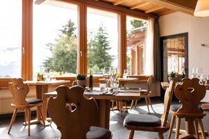 Un comedor con mesas y sillas de madera, amplias ventanas que ofrecen vistas a árboles y montañas.
