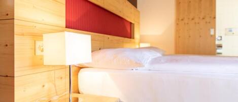 Una habitación de madera con una cama, una mesita de noche con una lámpara y un cabecero rojo.