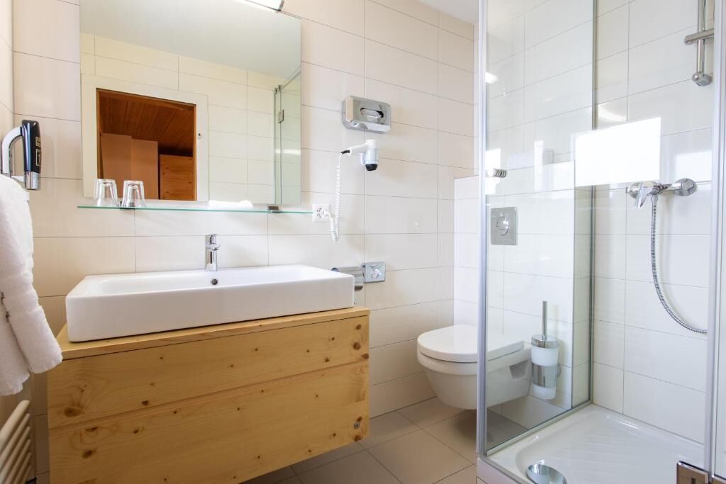 Un baño moderno con ducha acristalada, lavamanos blanco y tocador de madera.