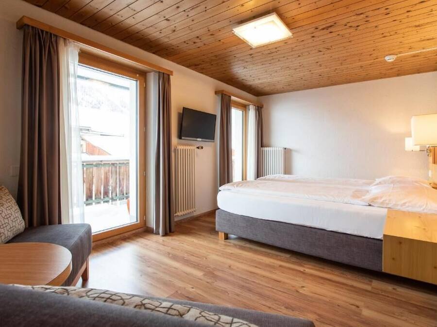 A bedroom with a bed, a TV, a sofa, and a window with curtains.