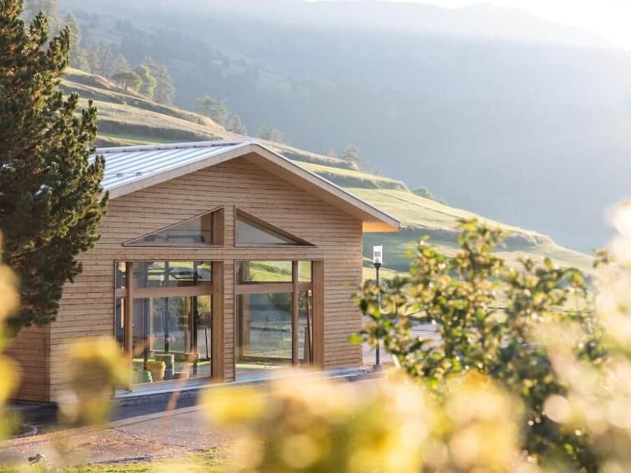Un edificio moderno con ventanas amplias y un techo inclinado, rodeado de entorno natural.