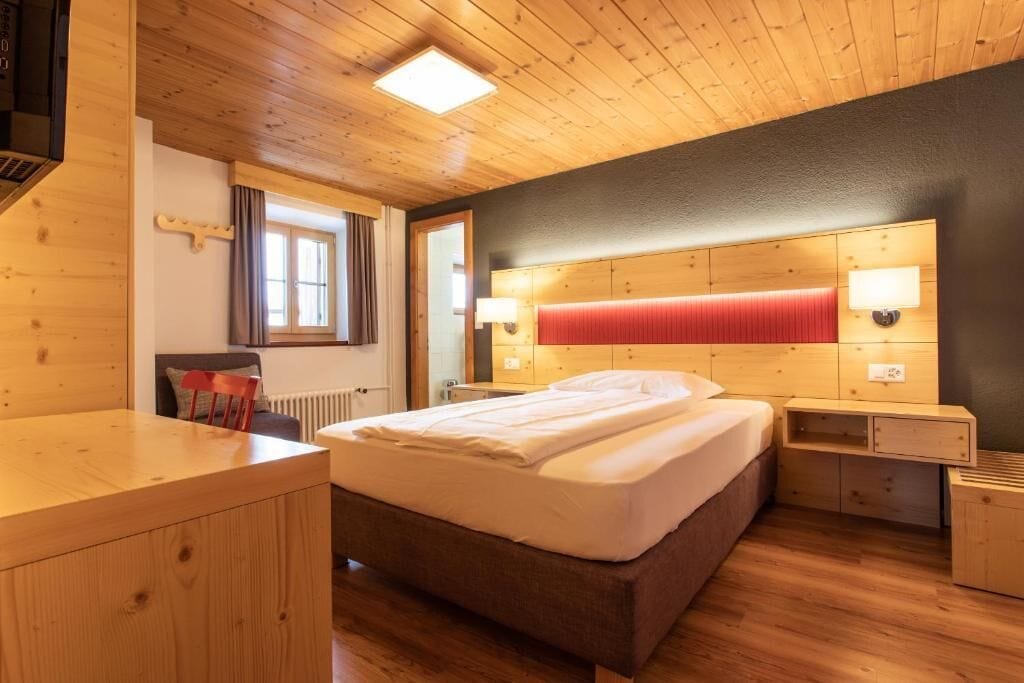 A wooden-floored bedroom with a bed, bedside tables, and a window.