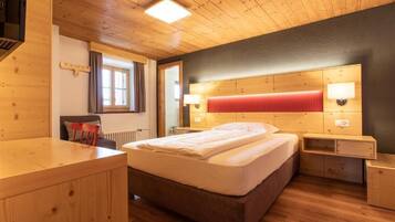 A wooden-floored bedroom with a bed, bedside tables, and a window.