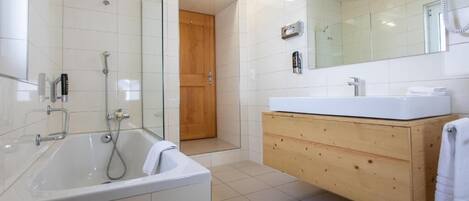 Un baño moderno con ducha envuelta en vidrio, una bañera blanca y un mueble de tocador de madera con lavamanos.