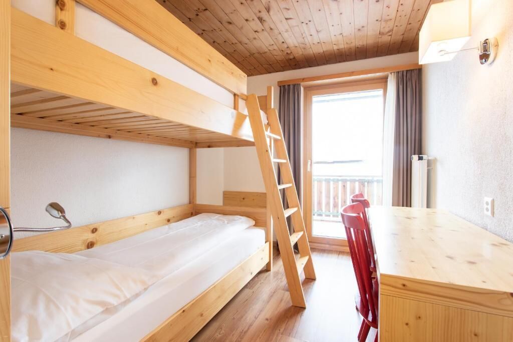 Dormitorio con literas, una escalera de madera, una mesa y sillas.