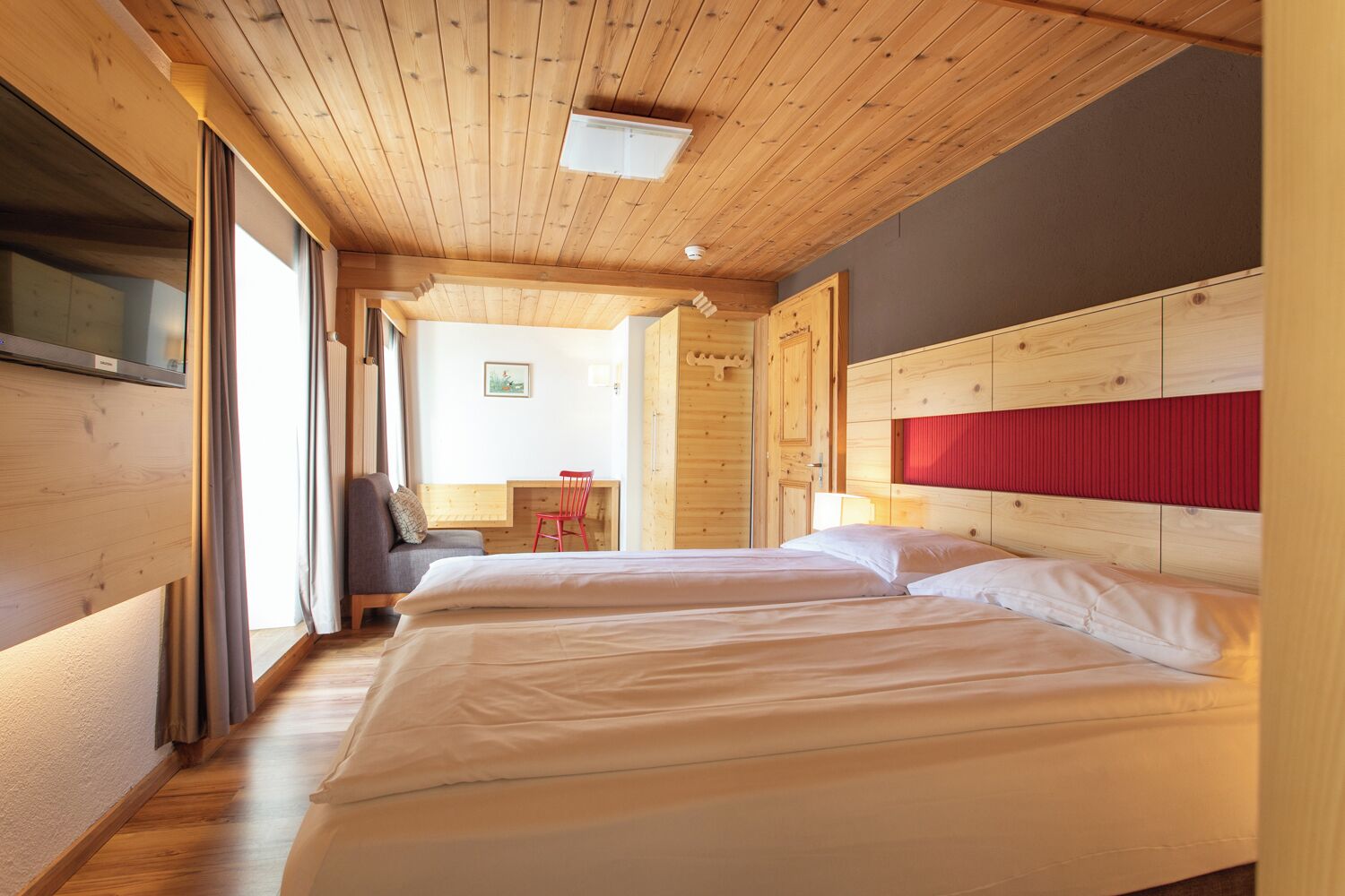A hotel room with wooden ceilings, two beds, a TV, and a small desk with a chair.