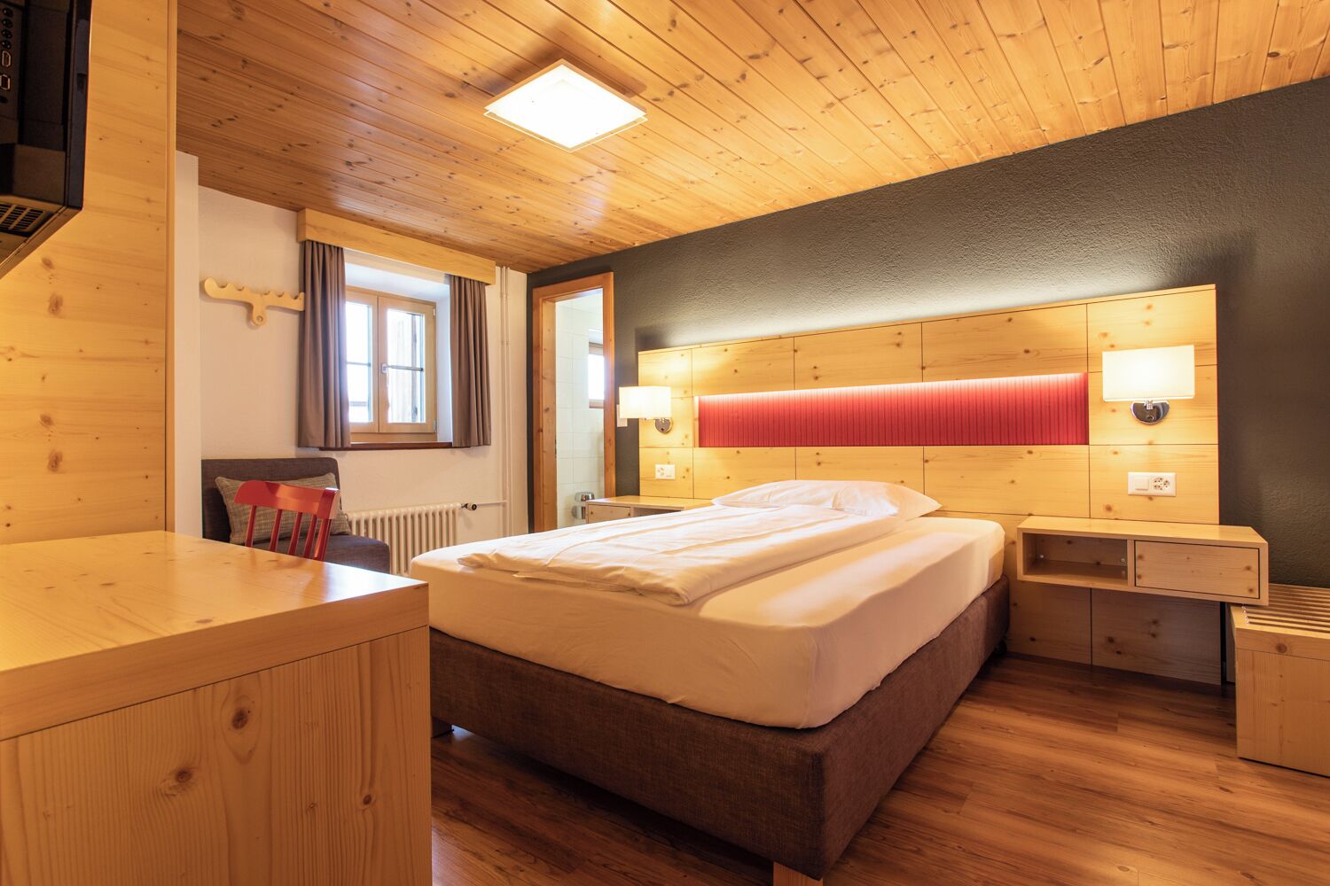 Une chambre avec un plancher en bois, un lit, des tables de chevet et une tête de lit rouge.