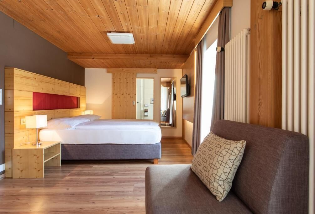 Una habitación de hotel con techo de madera, una cama, un sofá y una mesita de noche con lámpara.