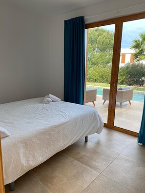 Une chambre avec un lit et une porte-fenêtre coulissante donnant sur un espace piscine équipé de chaises longues.