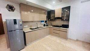 Een moderne keuken met een roestvrijstalen koelkast, beige keukenkastjes, een zwarte magnetron en een spoelbak met kraan.