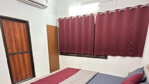 A bedroom with a bed, a window with curtains, an air conditioning unit, and a door. - The Vow Cartel Ananta (Varanasi)