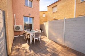 Un patio con mesa y sillas, una ventana y una cerca blanca.