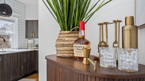Baaritiskialueella on pullo Maker’s Mark -viskiä, punottu kori, jossa on vihreitä kasveja, sekä kaksi kristallilasia puisen tiskin päällä.